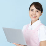 パソコンを手に持ちながらこちらを向いて微笑む医療従事者