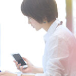 スマホを片手にパソコン画面を見つめる女性