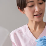 歯の模型を使いながら歯磨きの指導をする歯科クリニックスタッフとそれを聞く患者